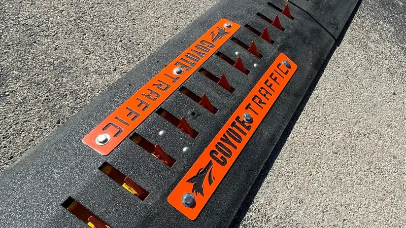 Coyote Traffic branded surface-mounted traffic spike section installed across an asphalt lane