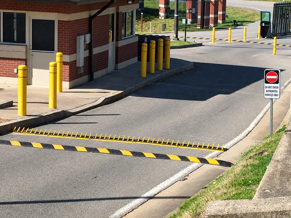 Aerial view of in-ground spikes across a guard-booth exit beside a warning sign