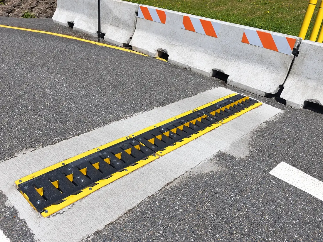 In-ground spikes set flush across a lane beside concrete barriers at a military gate