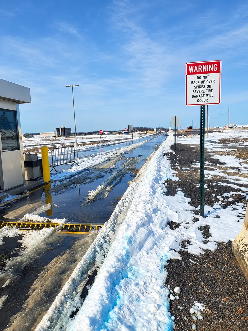 In-ground spikes beside a warning sign in a plowed winter exit lane