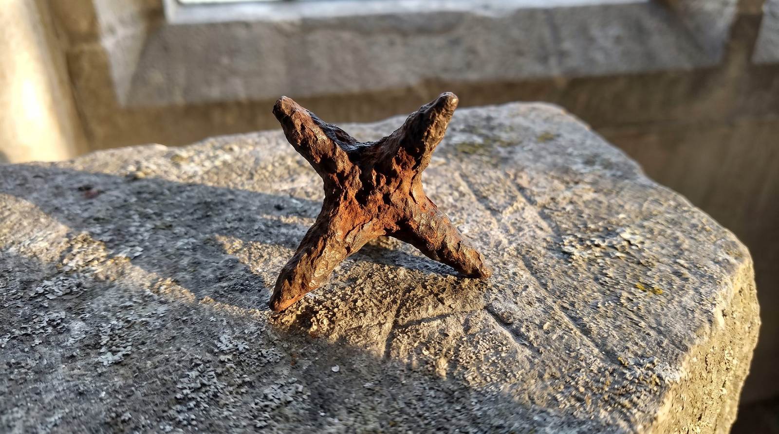 Rusted iron caltrop resting on a weathered stone block in low sunlight