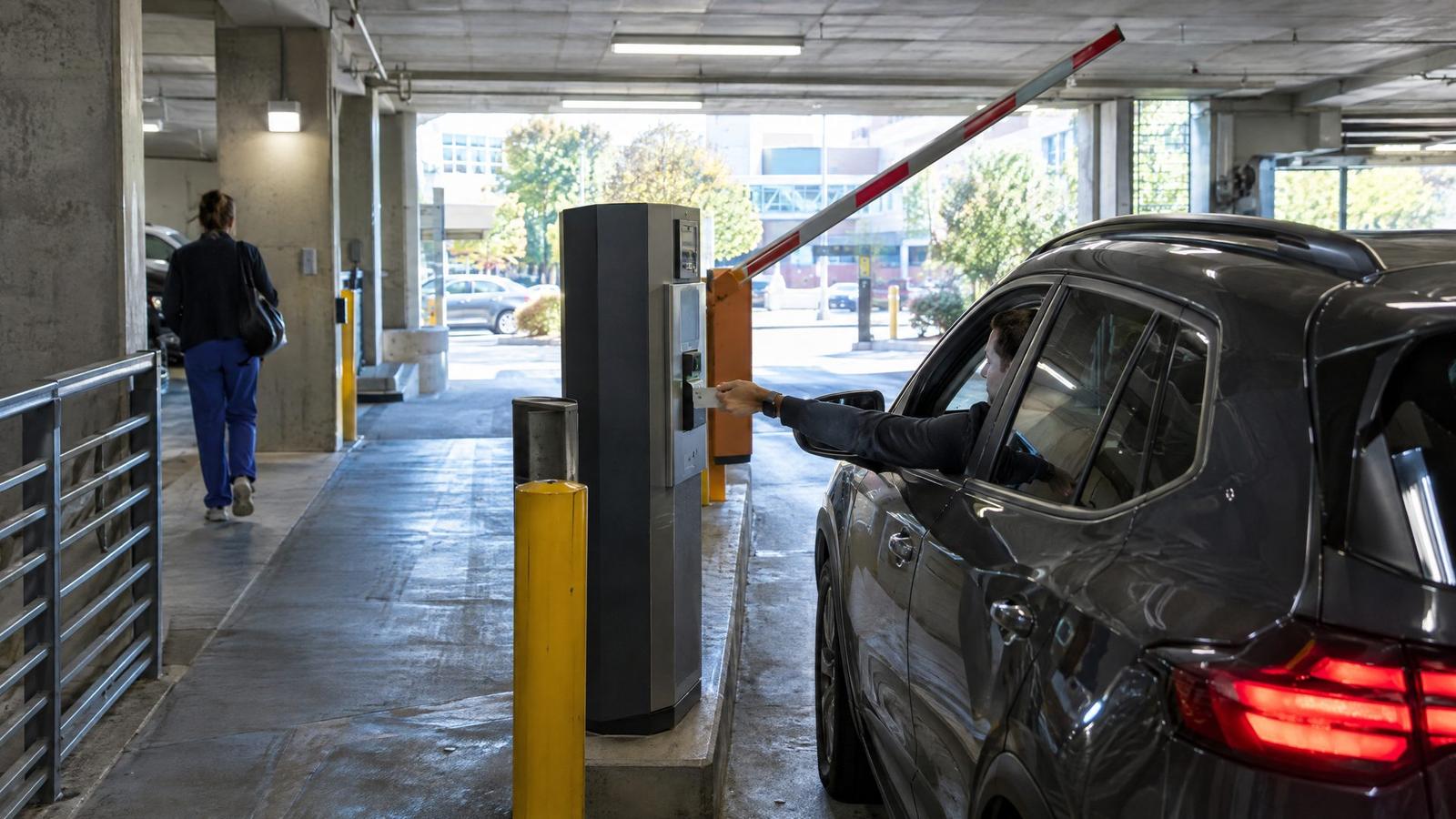 Driver badging in at a parking garage entry lane with a barrier arm and yellow bollard