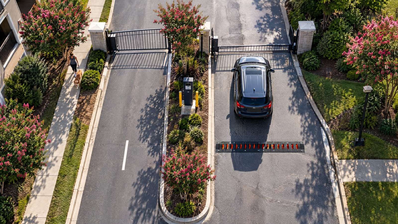 Aerial view of a gated residential entrance with a traffic spike strip across the exit lane