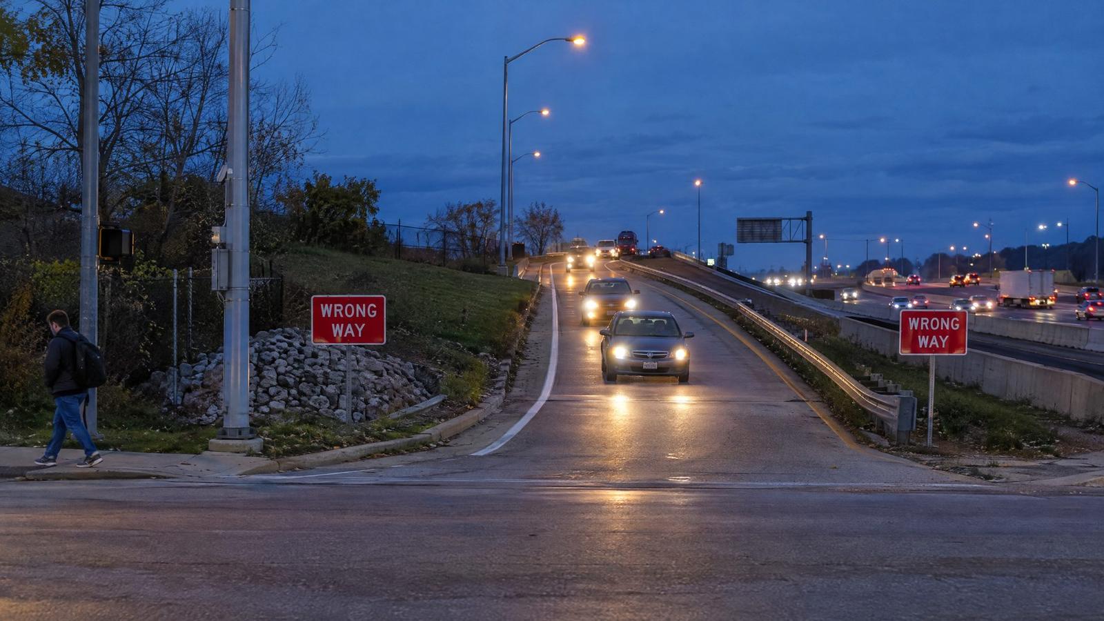 Wrong-way warning signs at a highway exit ramp at dusk with headlights approaching
