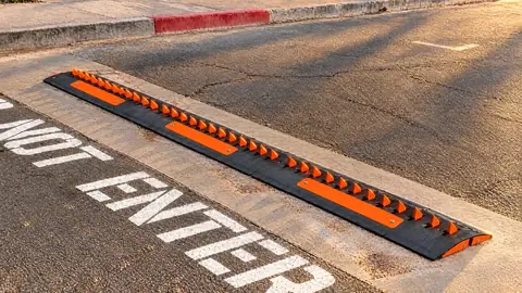 Surface-mounted traffic spike modules with orange teeth bolted at a one-way exit