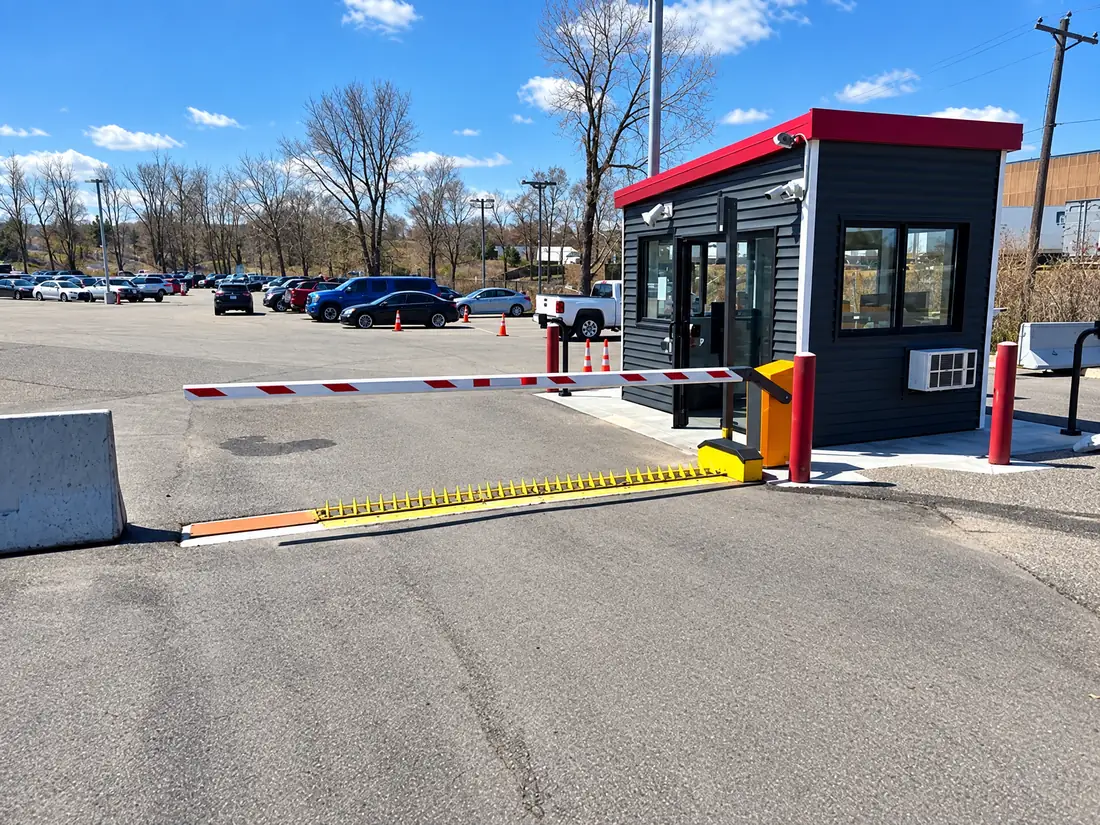 Motorized spike system beside a guard booth and gate arm at a parking-lot entry