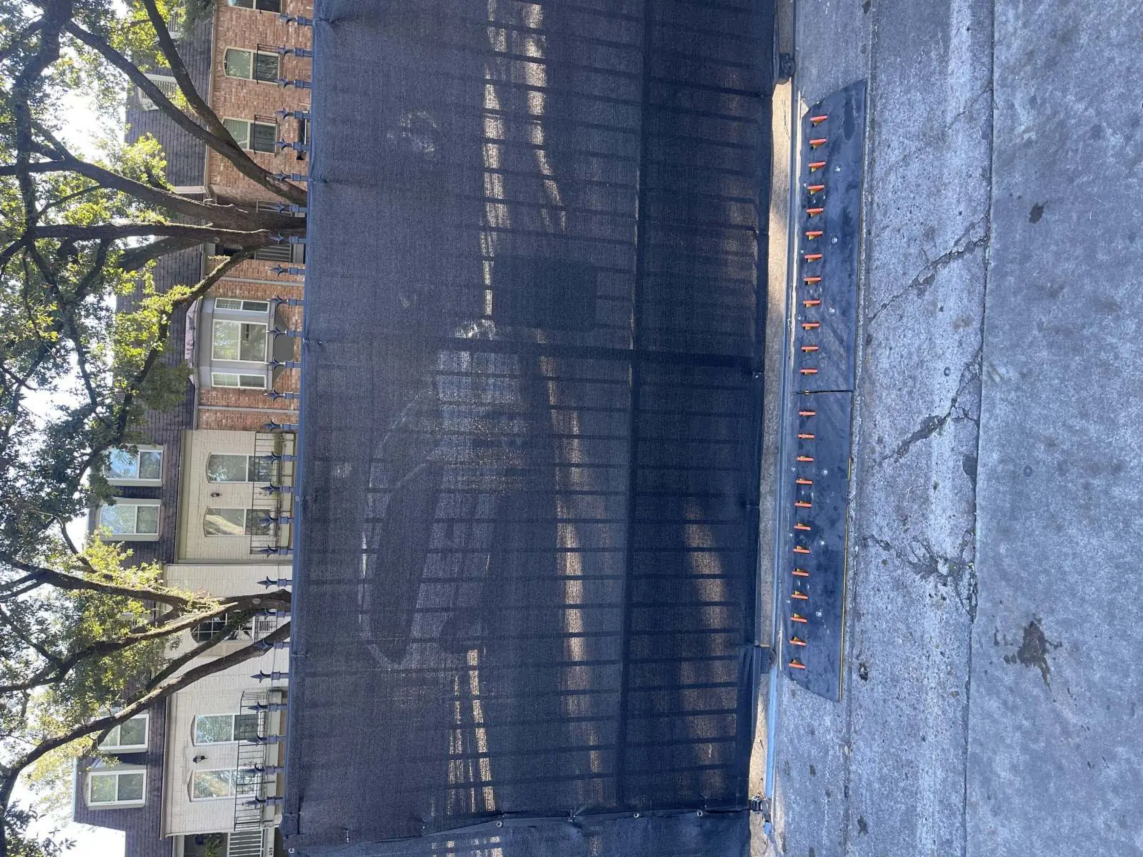 Traffic spike strips installed at a rolling gate on a sunny residential street lined with townhomes and trees