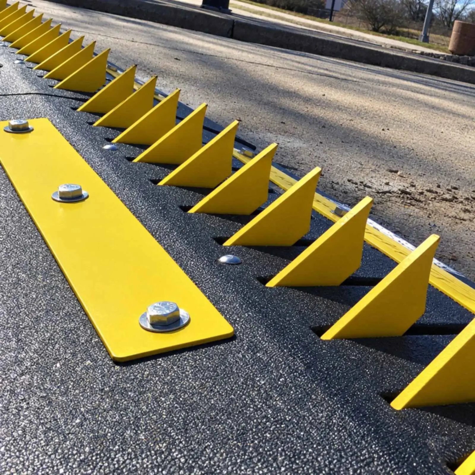 Close-up of yellow spring-loaded spike teeth on a black surface-mount ramp, each tooth's gentle slope facing left and steep point facing right