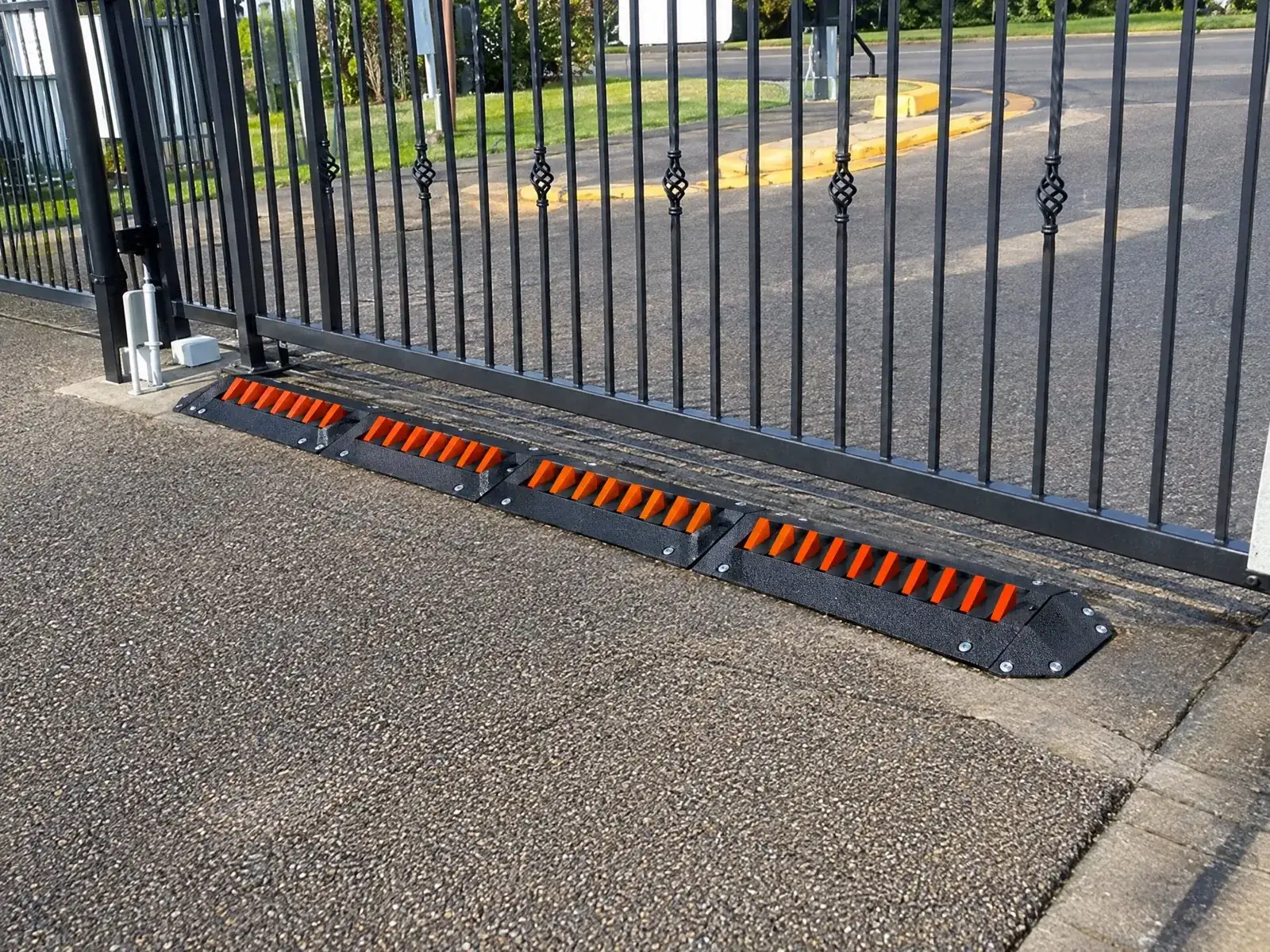 Four orange-tooth spike modules bolted in front of a wrought-iron sliding apartment gate