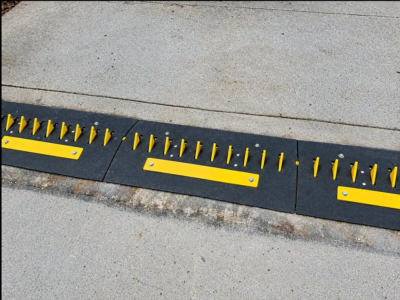 Yellow-tooth surface-mount spike modules joined end to end on a concrete driveway