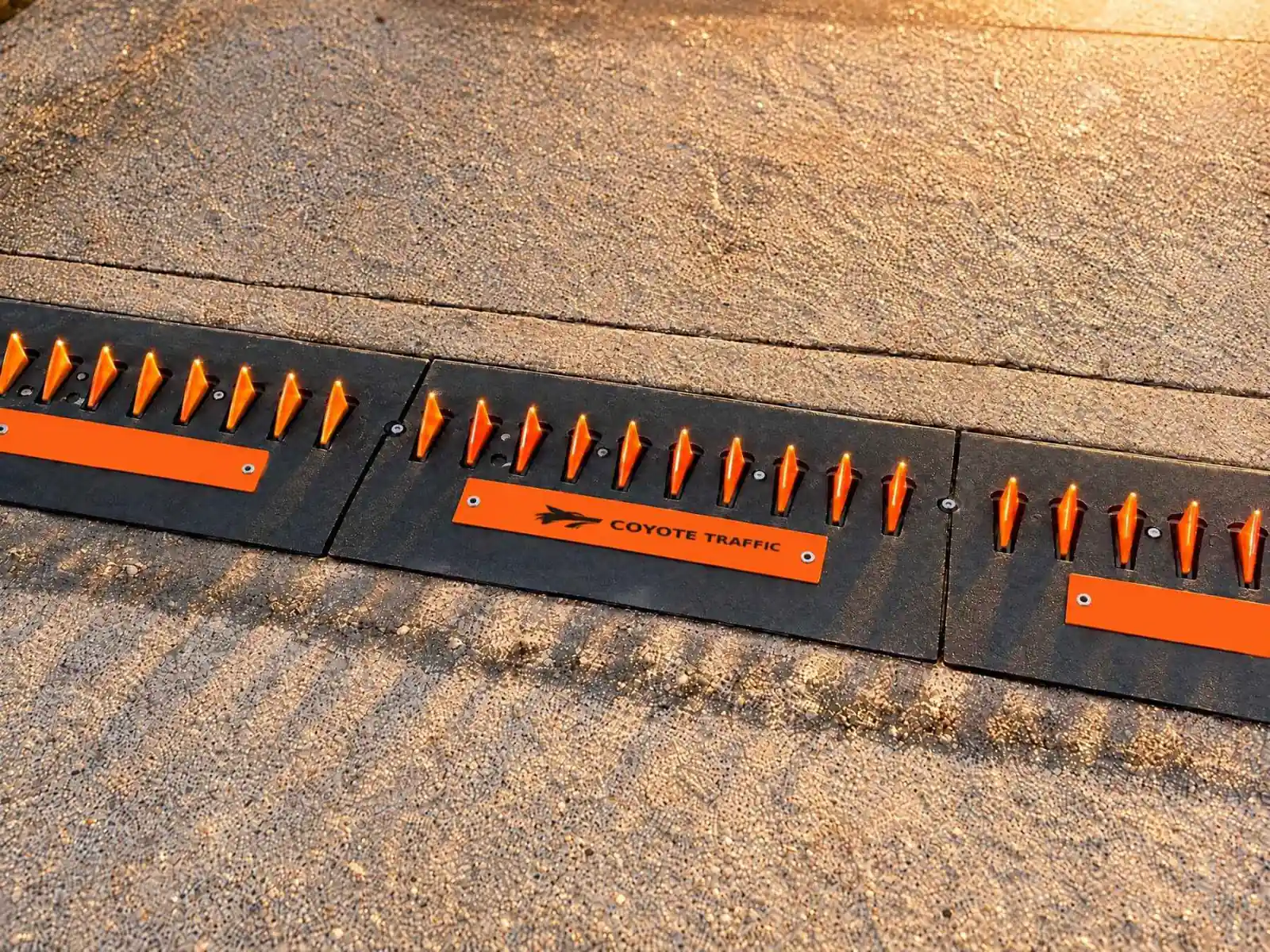 Three surface-mount spike modules with glowing orange teeth and Coyote Traffic faceplates on exposed-aggregate concrete at sunset